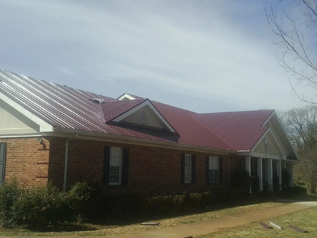 Red metal roof with gabled entries on a long brick building, from a Hail Damage Roof Repair job in Illiopolis