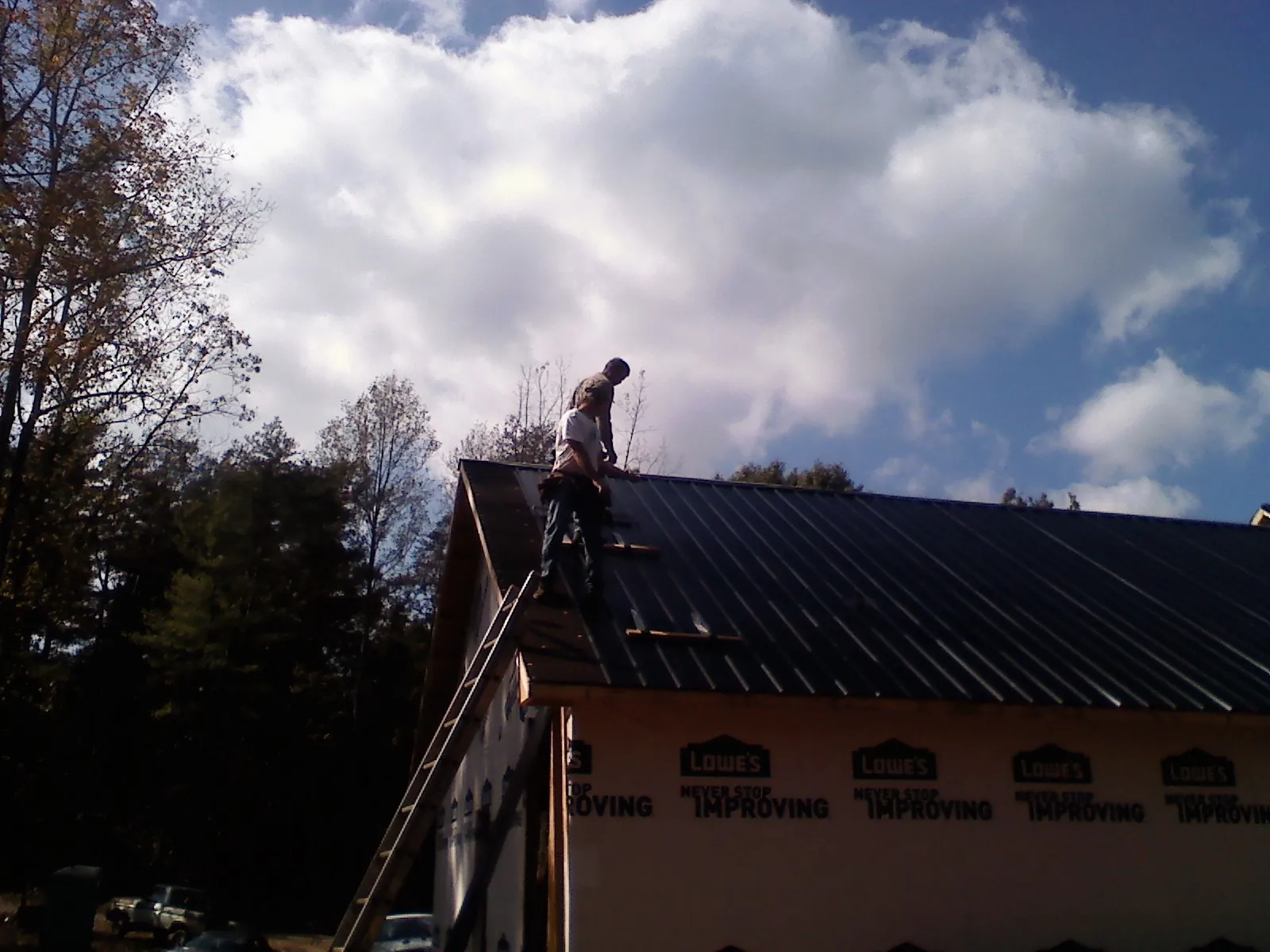 Roofer fastening dark metal panels high against a cloudy sky, from a Roof Inspection job in Illiopolis