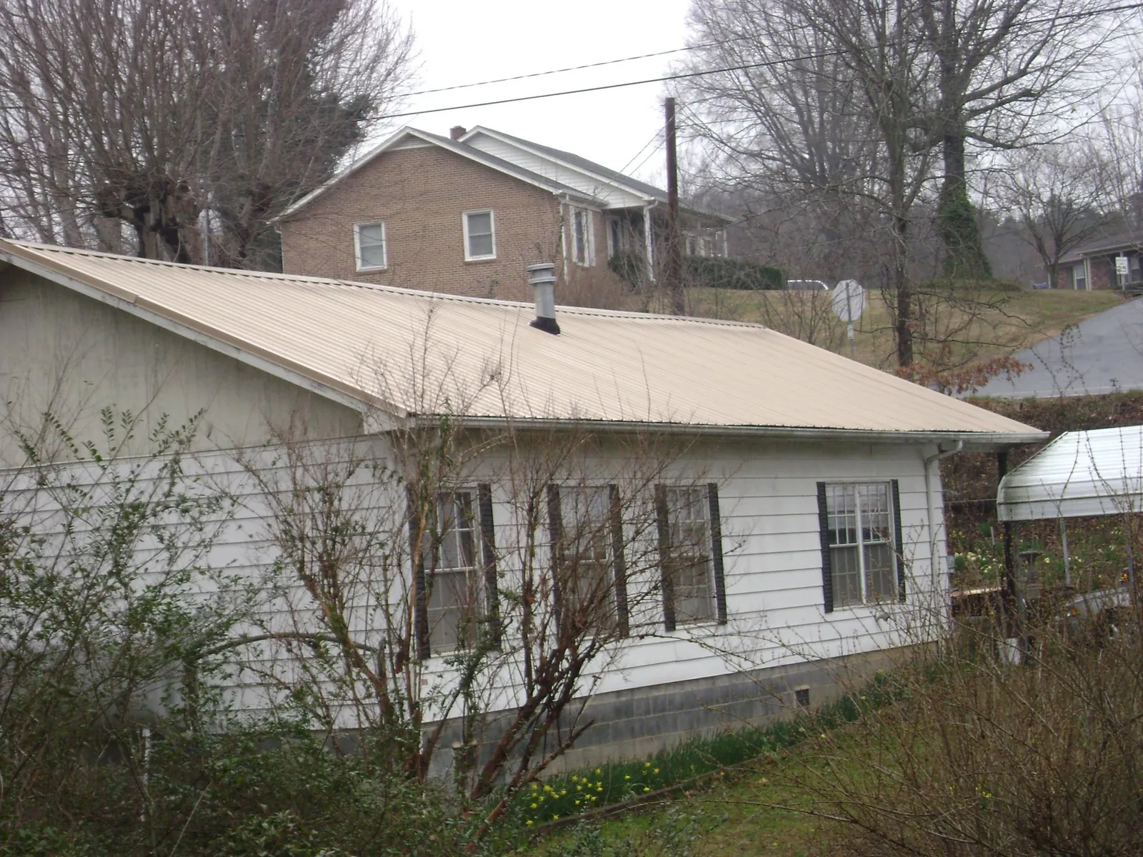 Tan metal roof on a white sided house set into a hillside — Commercial Roofing by Roofing Brothers in Illiopolis